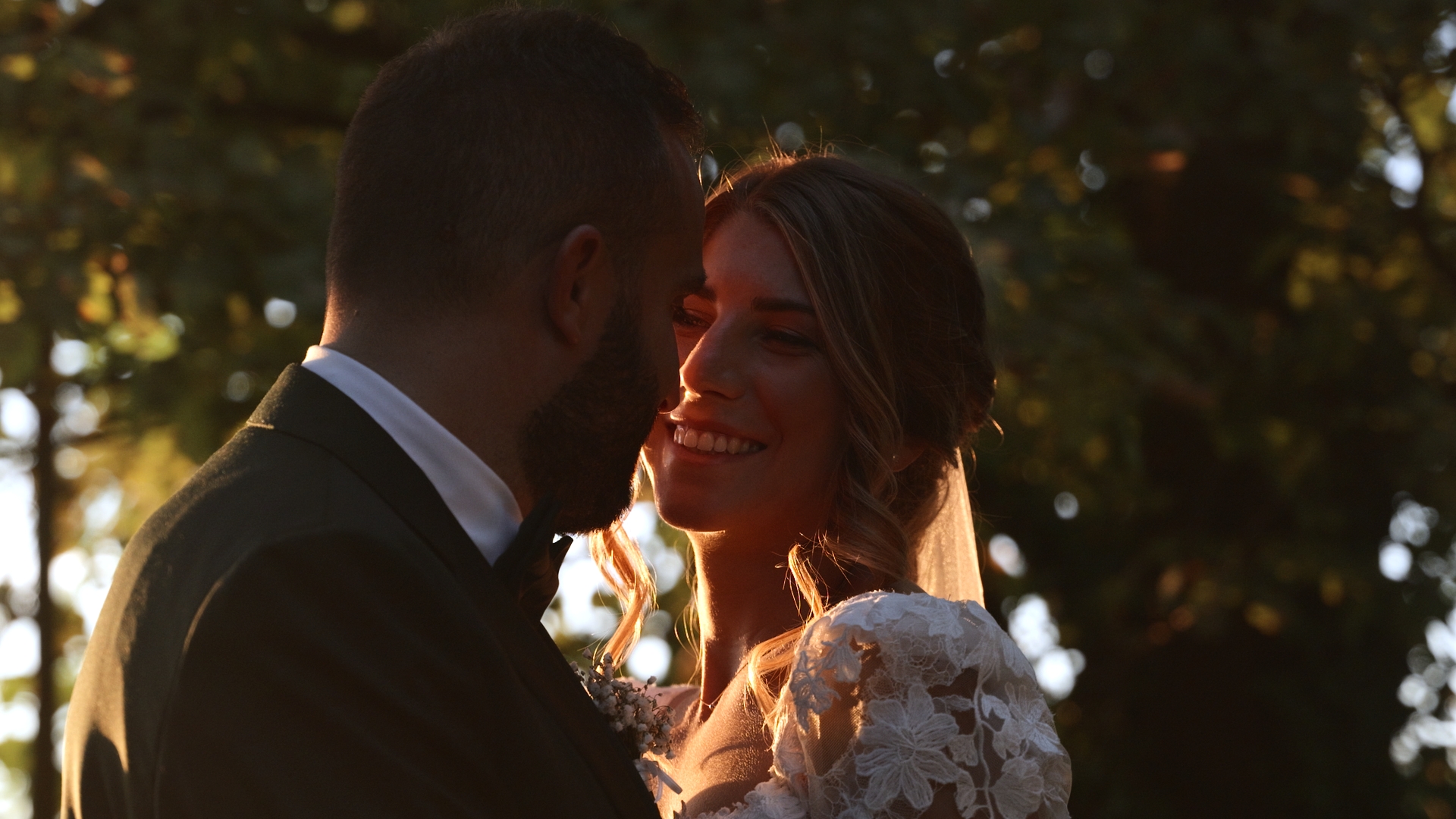 Sposa e sposo vicini al tramonto, i volti accarezzati da una luce dorata tra gli alberi