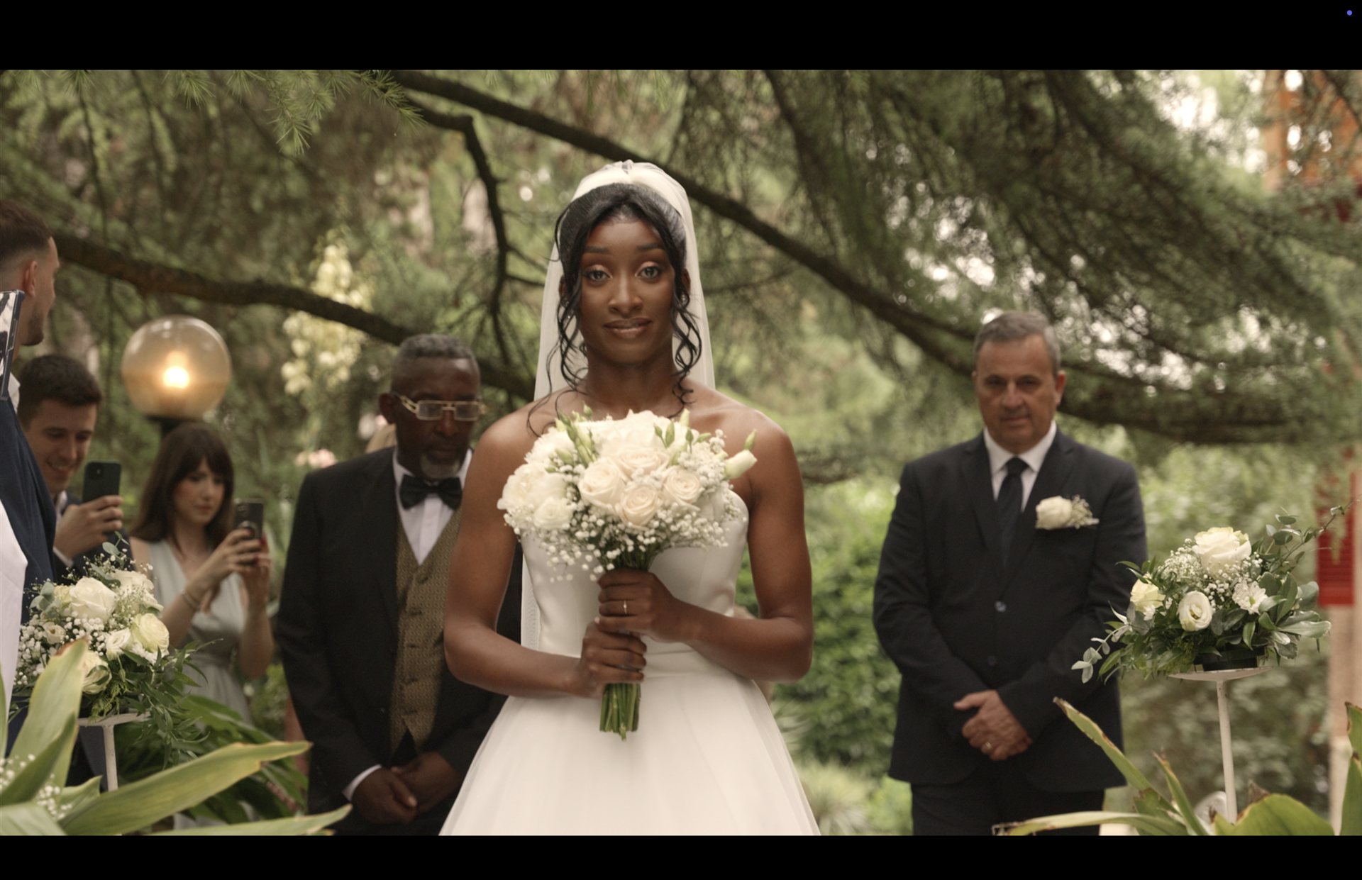 Sposa con bouquet di rose bianche all'ingresso della cerimonia, immersa nel verde del giardino