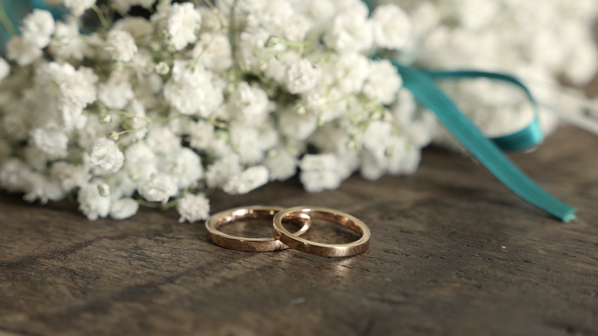 Due fedi dorate appoggiate su un tavolo di legno antico, accanto a un bouquet di fiori bianchi